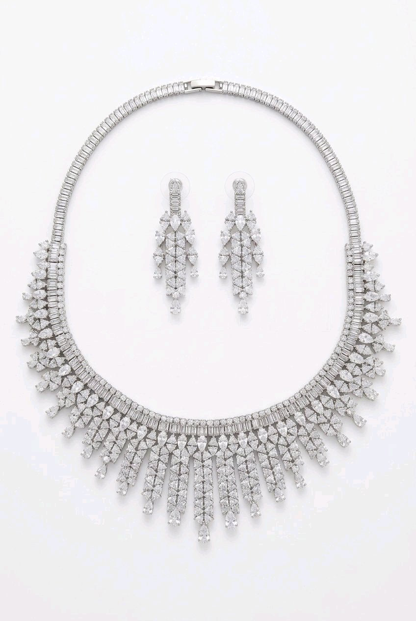 Grand Fringe Bib CZ necklace and chandelier earrings flat lay on white background